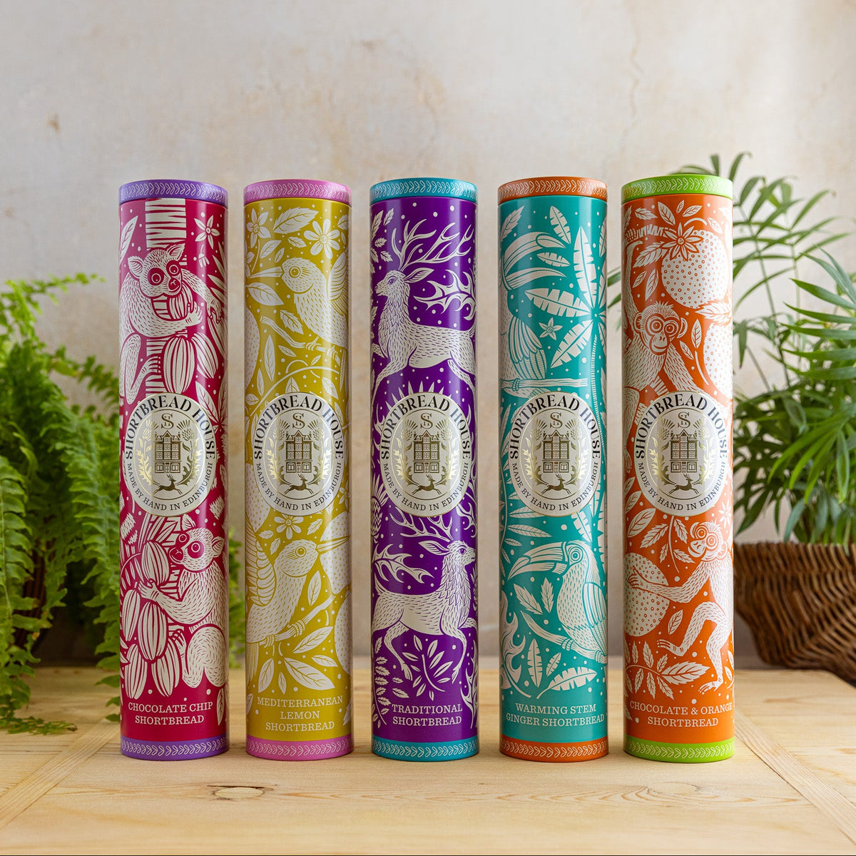 Five colorful shortbread tins with decorative labels on a wooden surface.