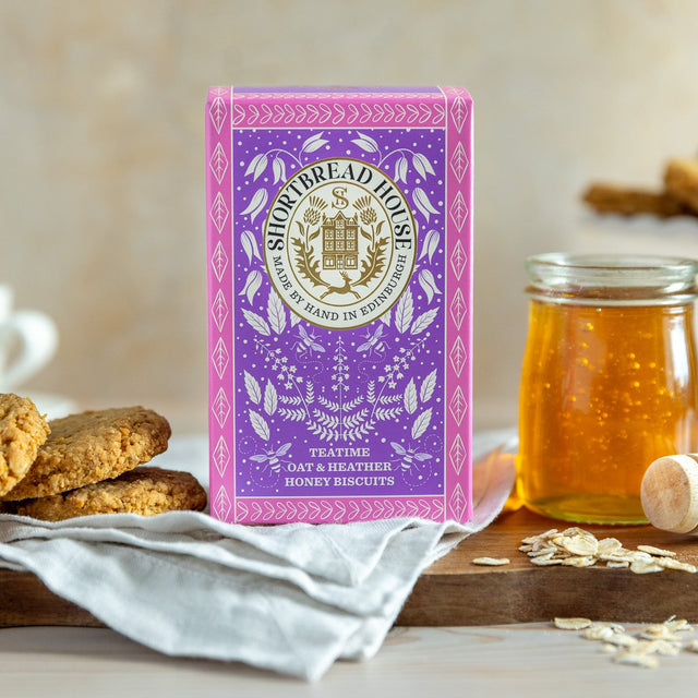 Box of Heather Honey Oaties with a jar of honey and biscuits on a wooden board.