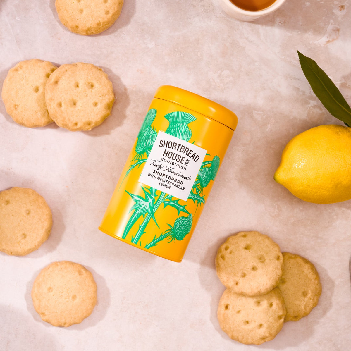 Yellow tin of Shortbread House lemon shortbread cookies with cookies and a lemon on a light background