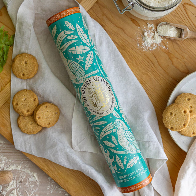 Tall tin with a blue toucan design on a chopping board with biscuits and flour