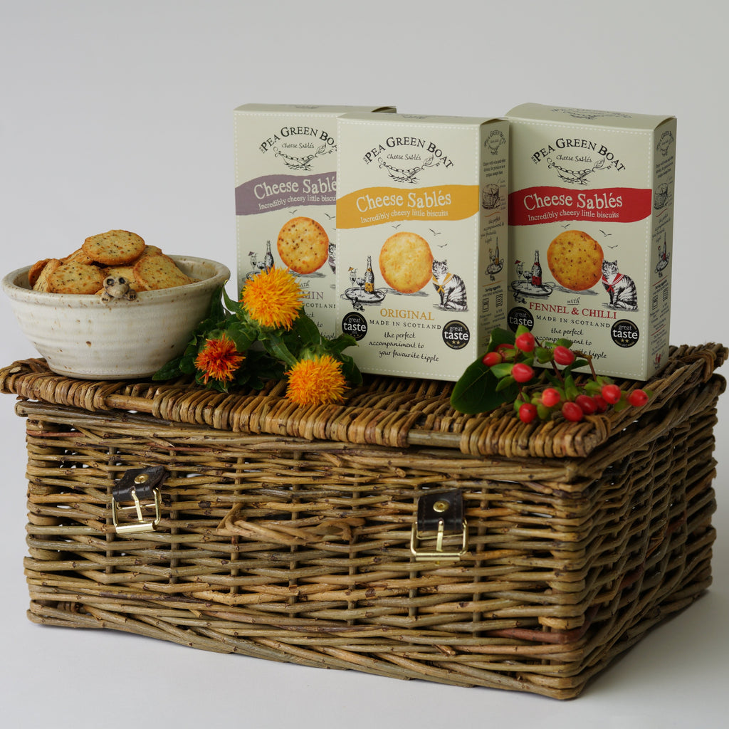 The three boxes of Cheese Sables from Pea Green Boat on top of a picnic basket with flowers.
