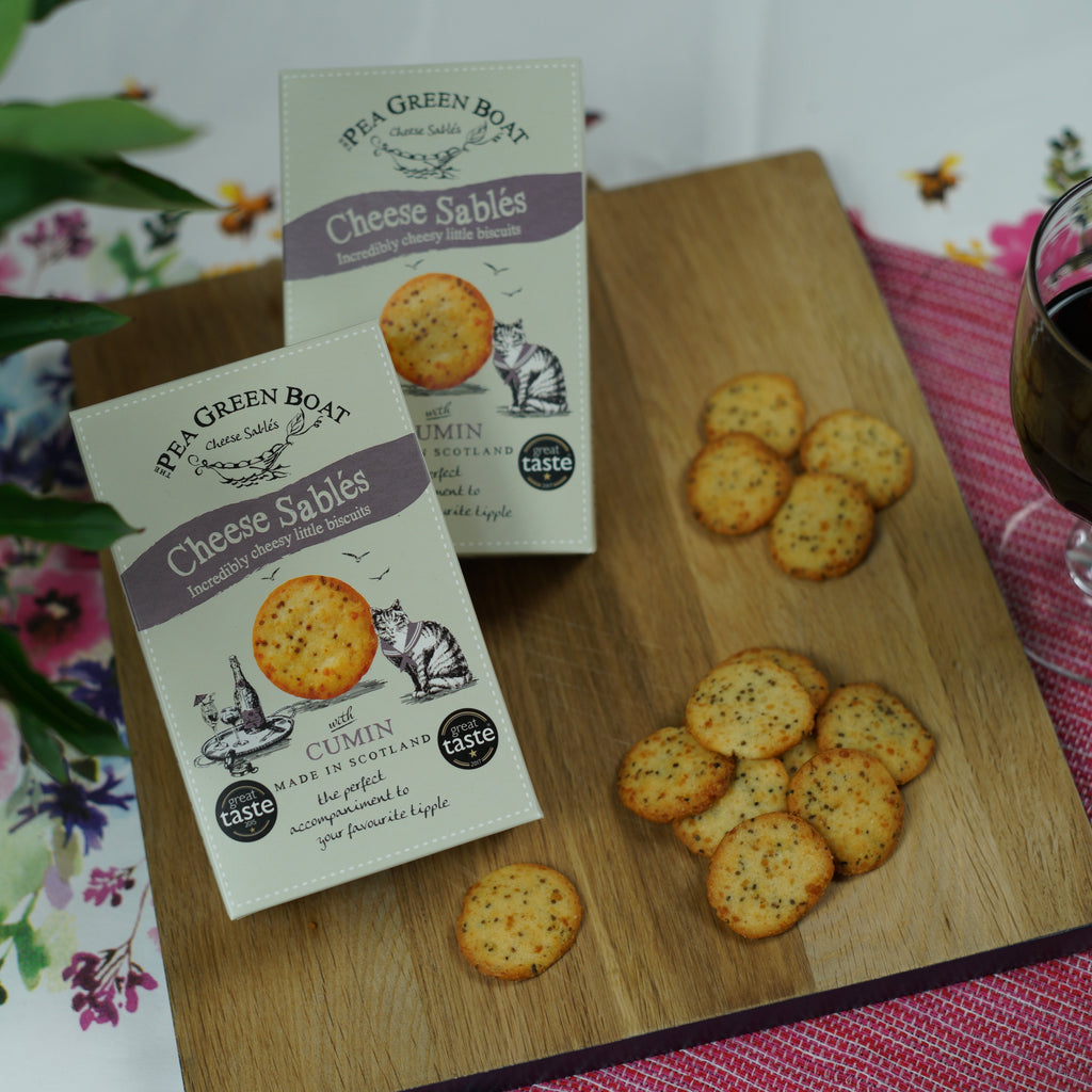 Two boxes of cumin cheese sables on a table, next to a glass of red wine and some cheese sables