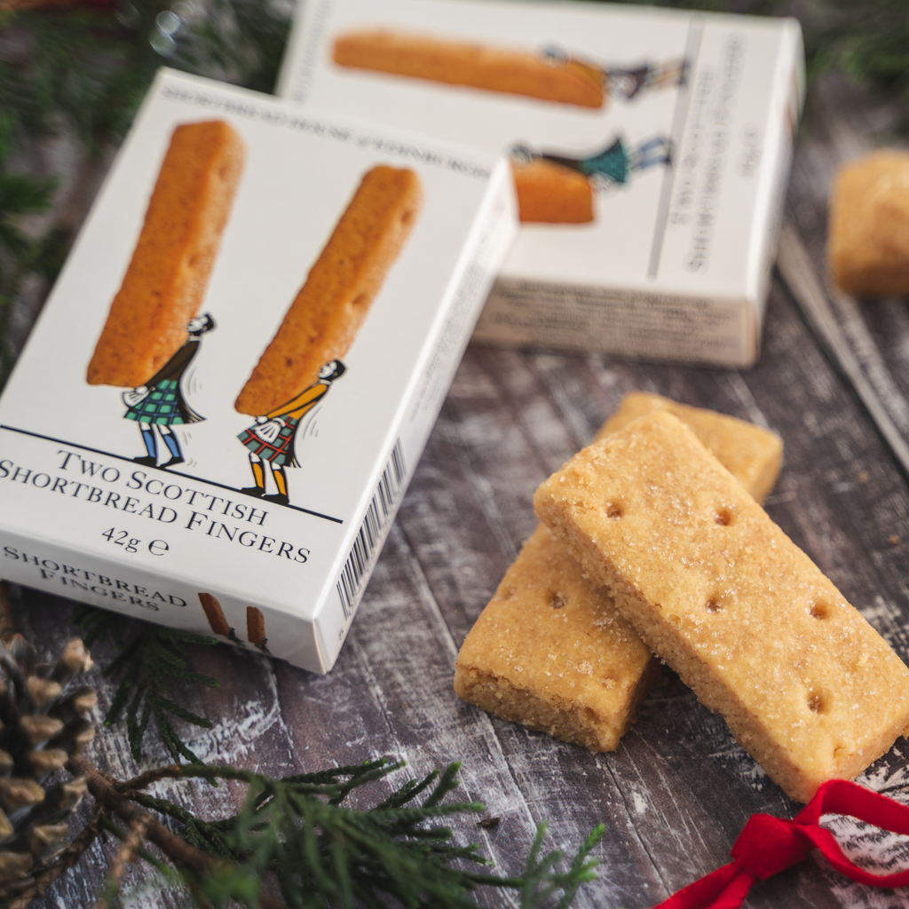 Two Scottish Shortbread Fingers on a wooden surface with packaging in the background.