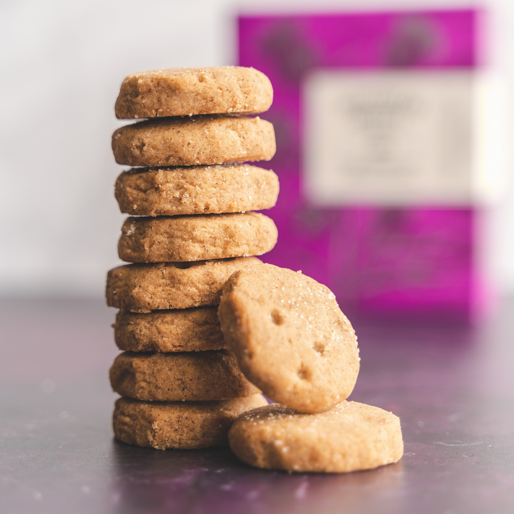Stack of round biscuits on a reflective surface with box of shortbread in the background