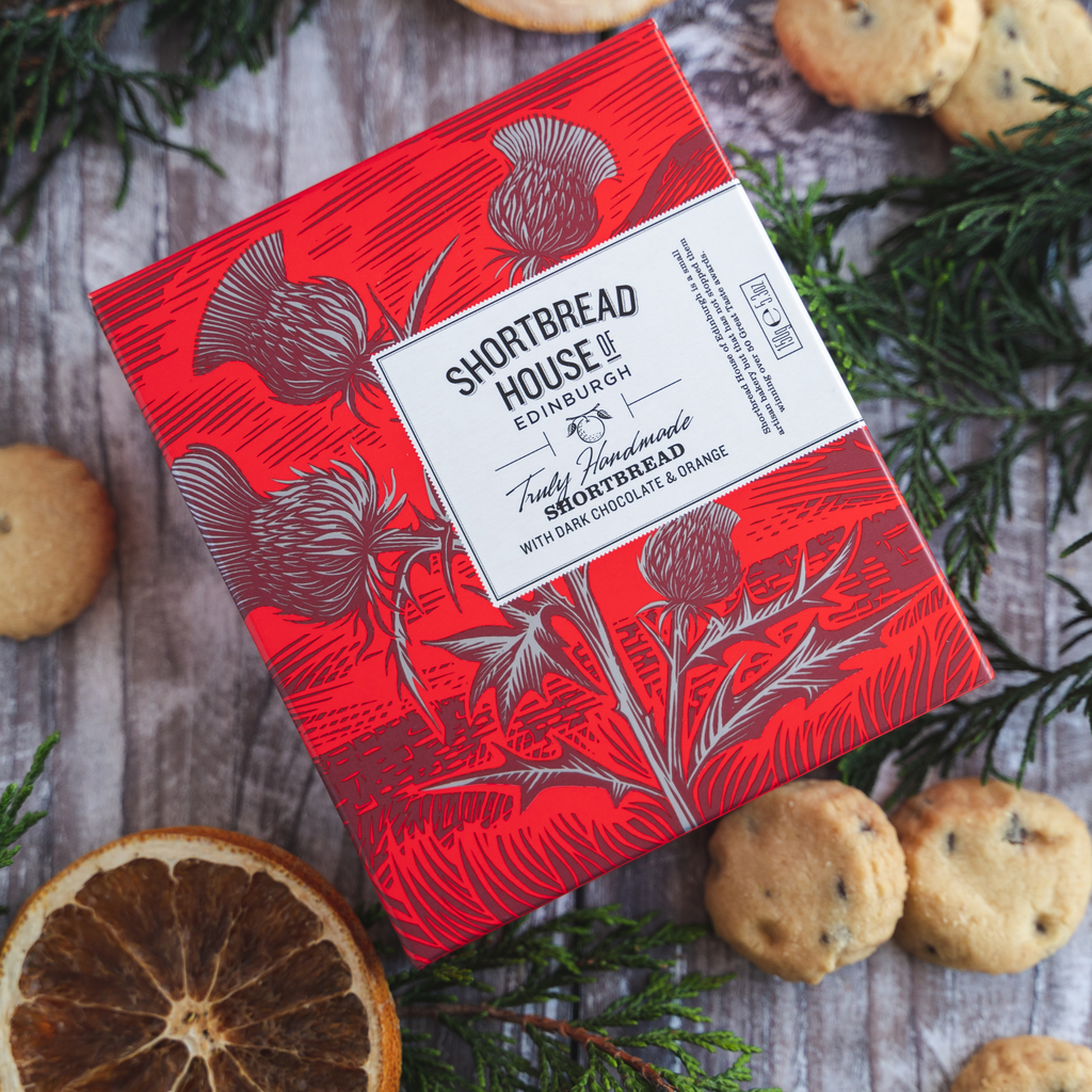 Red box of Shortbread House Edinburgh shortbread with biscuits and an orange slice on a wooden surface.