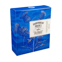 A rectangular blue box of Shortbread House of Edinburgh shortbread with macadamia notes, decorated with white illustrations of thistles and a central cream label.
