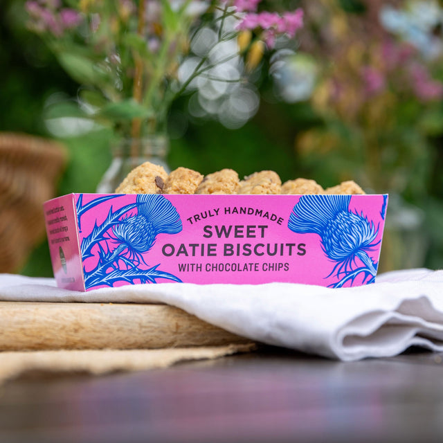 A pink tray of sweet oatie biscuits in an outdoor setting burred softly in the background, with 6 oatie biscuits showing from the top of the tray.