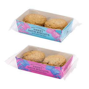 Two packaged boxes of Truly Handmade Sweet Oatie Biscuits shown on a white background, one with chocolate chips. The boxes have pink and blue packaging with thistle illustrations.