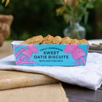 A blue tray of sweet oatie biscuits in an outdoor setting, with a wooden board and napkin underneath. In the tray there are 6 oatie biscuits.