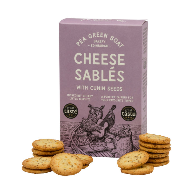 Box of Cheese Sablés with Cumin Seeds from Pea Green Boat Bakery Edinburgh, surrounded by cheese biscuits. The packaging features an owl playing a guitar in a boat.