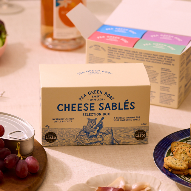 Box of Cheese Sablés from Pea Green Boat Bakery on a table with snacks and drinks.