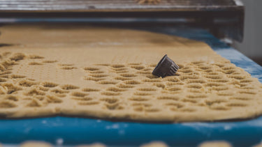A close-up of a dark metal cookie cutter resting on a sheet of textured beige dough on a blue surface.