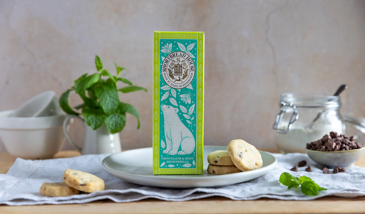 Green box of shortbread on a plate with mint, chocolate and kitchen items in the background