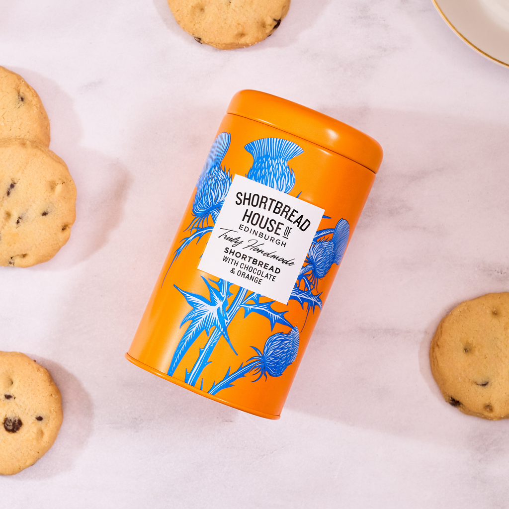 Orange cookie tin with blue thistle design and 'Shortbread House Edinburgh' label, surrounded by biscuits on a white surface.