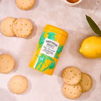 Yellow tin of Shortbread House lemon shortbread cookies with cookies and a lemon on a light background