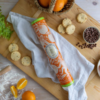 An orange shortbread tin with a monkey design on a wooden chopping board surrounded by cookies, oranges and chocolate