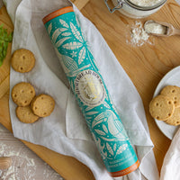 Tall tin with a blue toucan design on a chopping board with biscuits and flour
