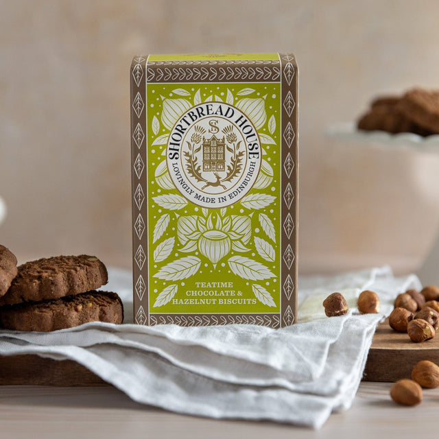 Green box of Hazelnut and Chocolate Biscuits with cookies and nuts on a wooden board