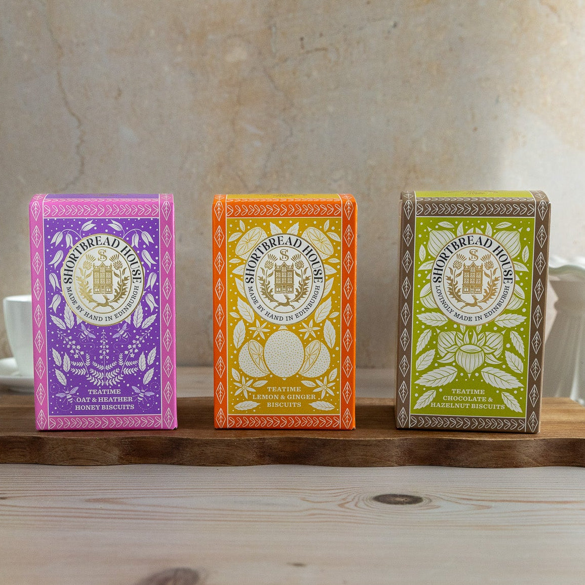 Three colourful sweet biscuit boxes on a wooden stand with a neutral background