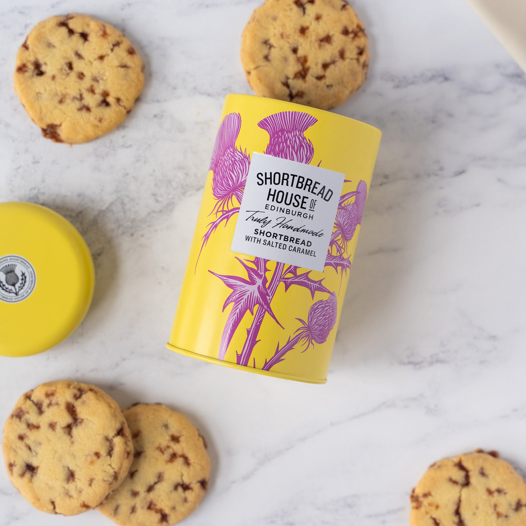Yellow tin of Shortbread House shortbread biscuits on a marble surface with biscuits around it.