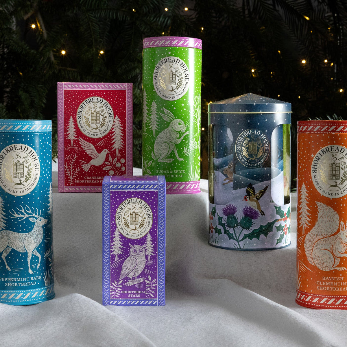Collection of colourful christmas tins with nature-themed designs on a white surface with a Christmas background.