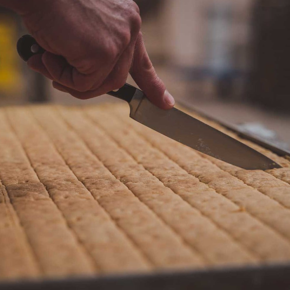 A tray of shortbread fingers being hand cut with a knife