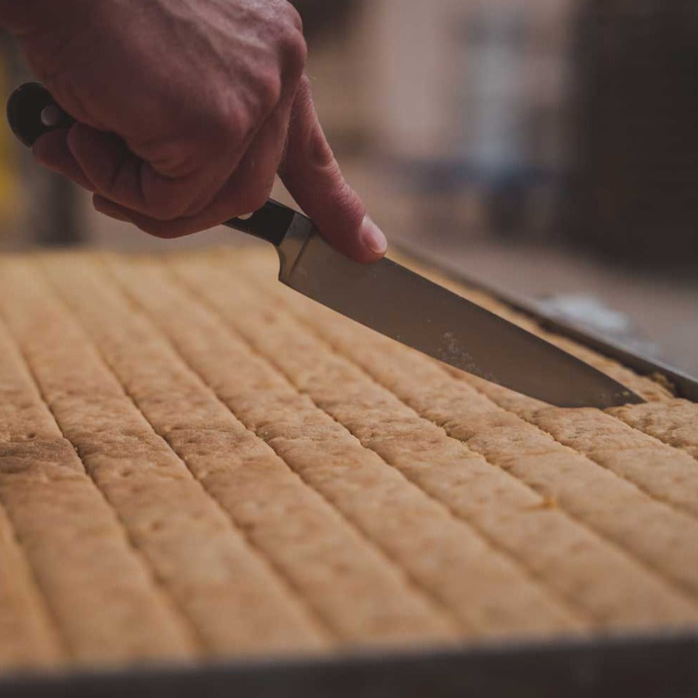 A tray of shortbread fingers is being hand cut with a knife