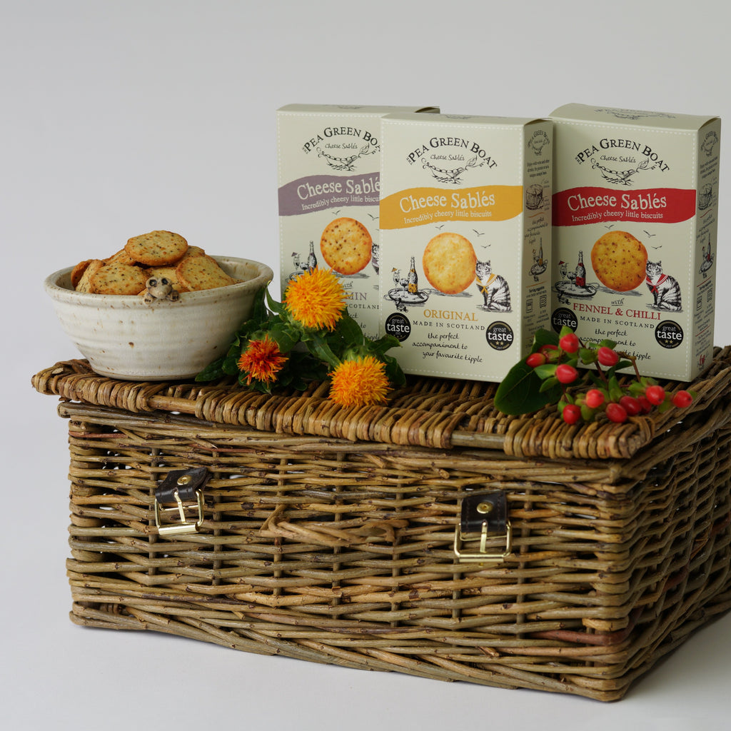 The three boxes of Cheese Sables from Pea Green Boat on top of a picnic basket with flowers.